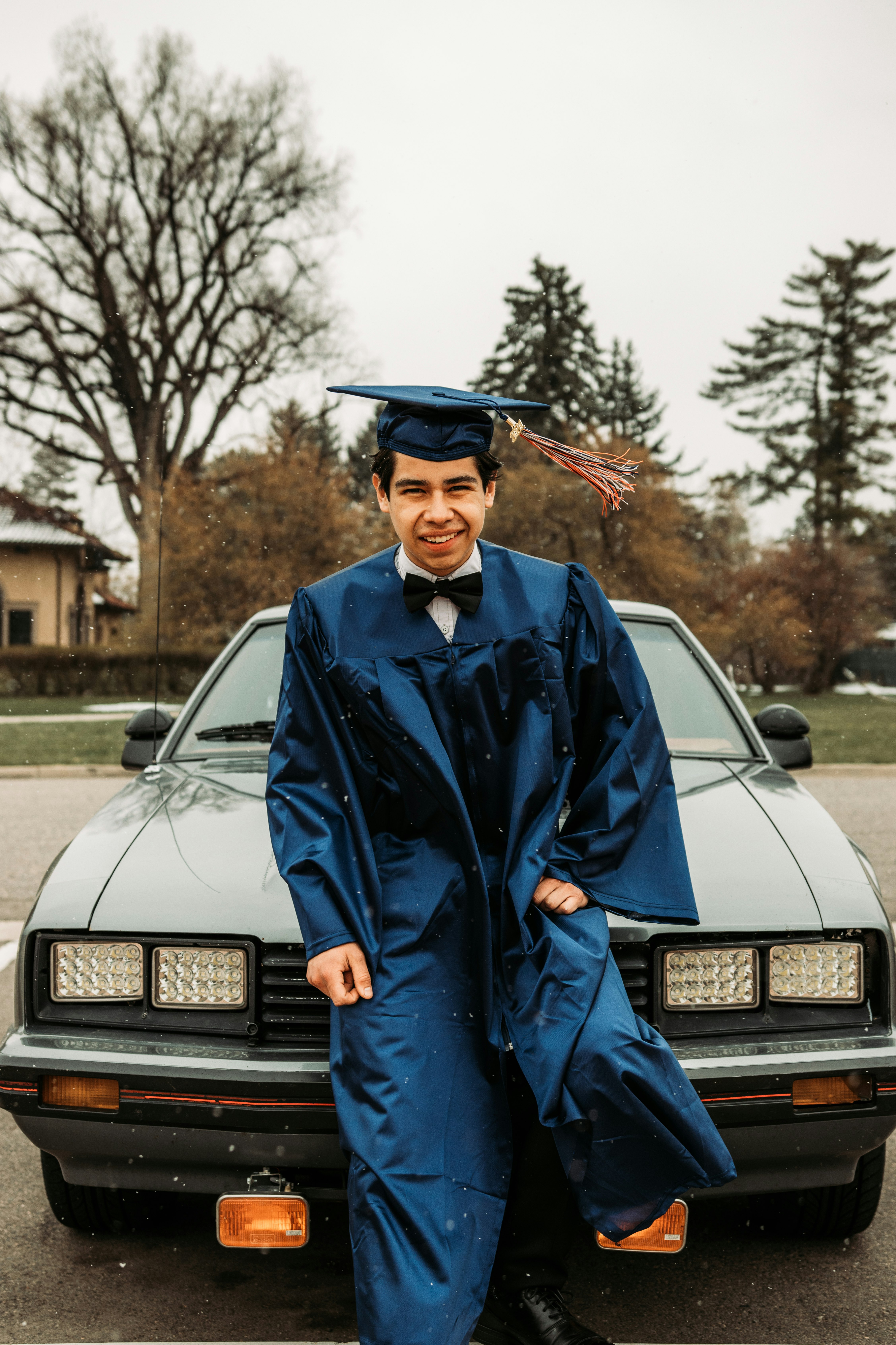 man in blue academic gown standing beside white car